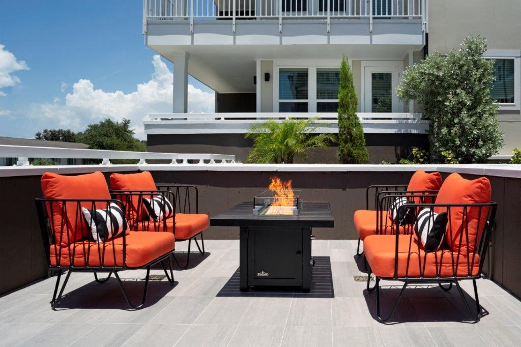 a fire pit on a patio with orange chairs and a black table