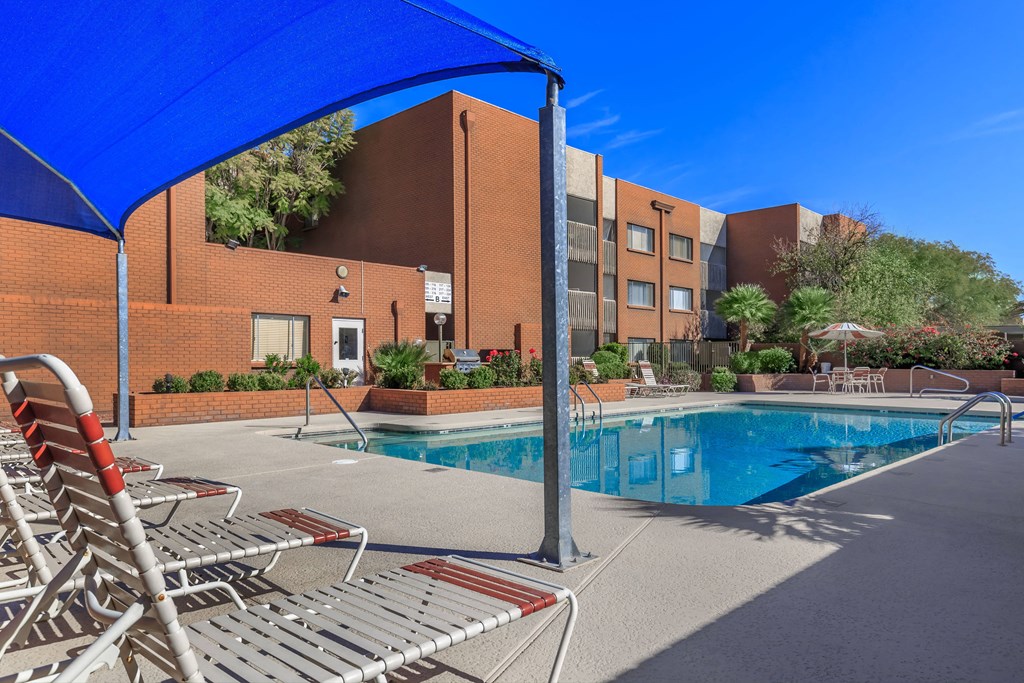 A pool area with sun loungers and a blue canopy.
