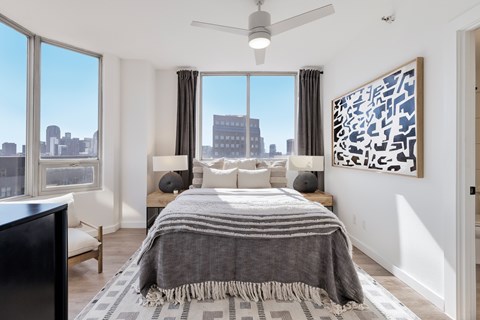 A bedroom with a large bed and a city view through the window.