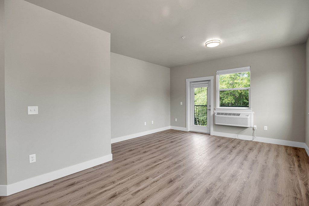 A room with wooden flooring and a window with a view of greenery outside.