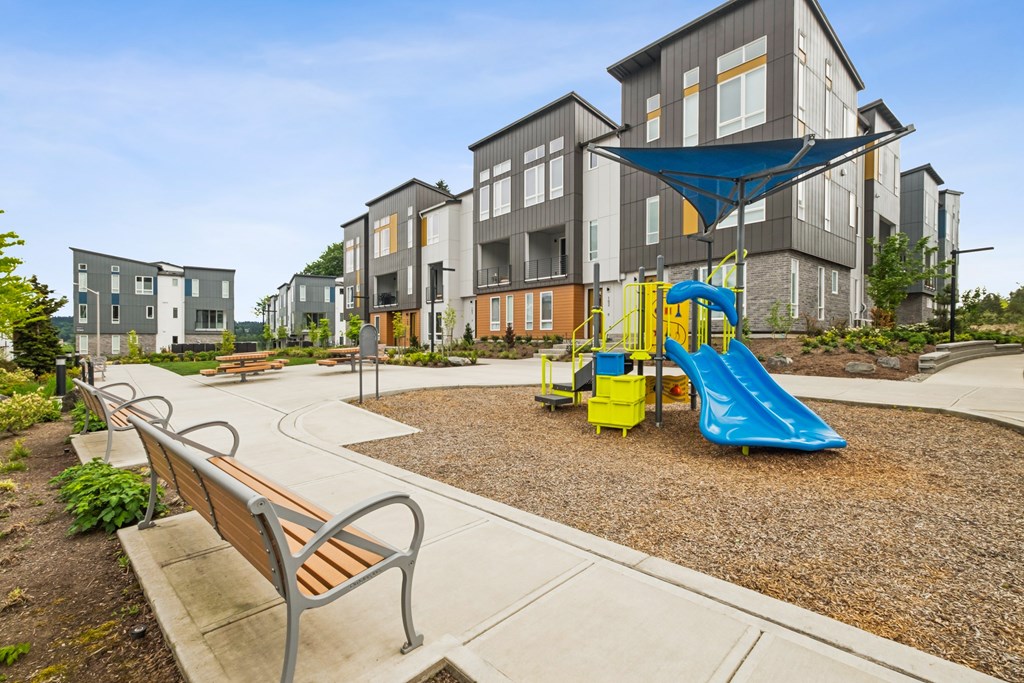 A playground with a blue slide and a bench in front of apartment buildings.