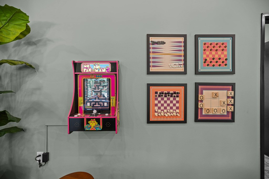 A wall with a pinball machine and several framed pictures.
