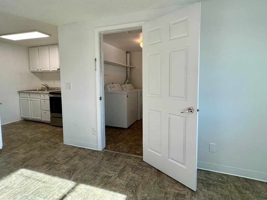 an open door leading into a kitchen with white cabinets and a refrigerator