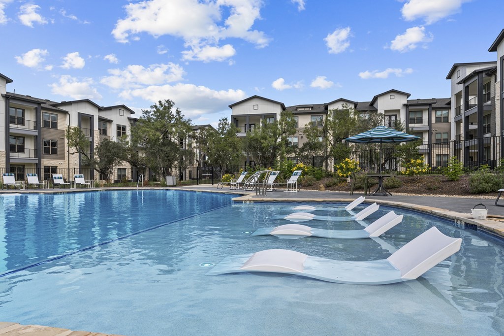 A swimming pool with lounge chairs and apartment buildings in the background.