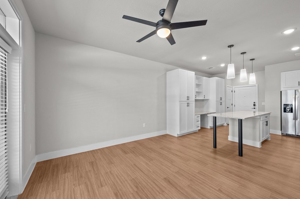 a living room and kitchen with white walls and a ceiling fan