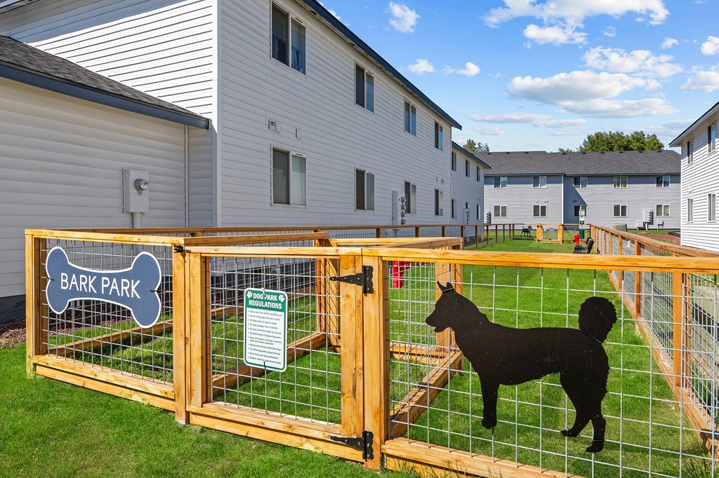A dog park sign is on a fence in front of a grassy area.