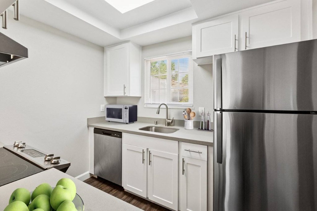 A kitchen with a refrigerator, sink, and green apples on the counter.