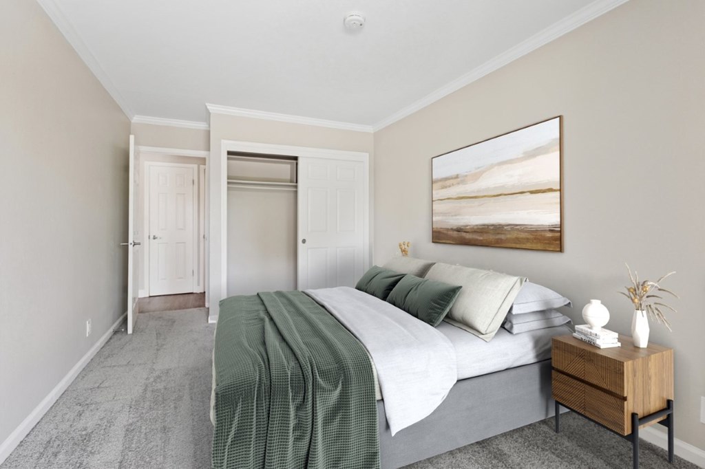 A bedroom with a bed, nightstand, and a painting on the wall.