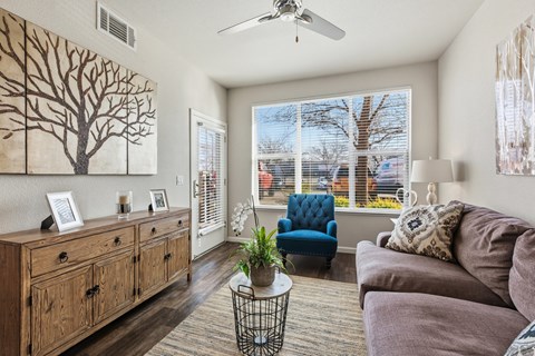 A living room with a blue chair and a painting of a tree on the wall.