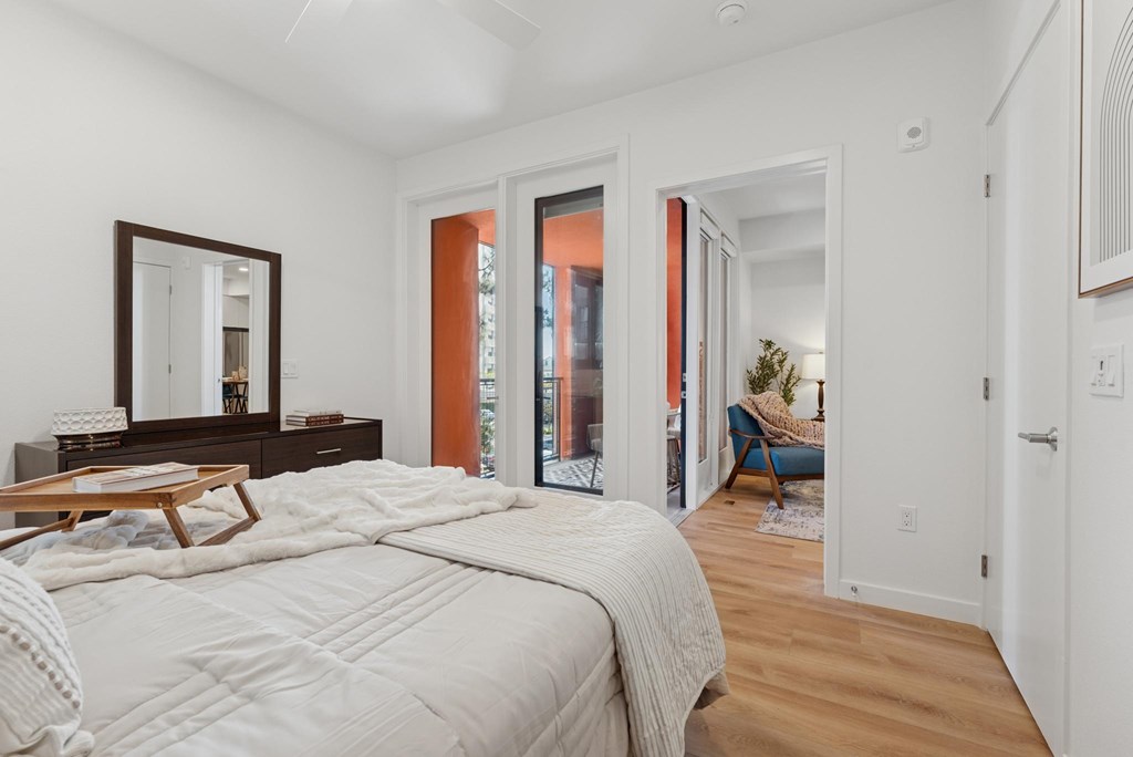 OnyxOnPark_SanDiego_CA_Model_1BR_ A bedroom with a large bed and a mirror on the dresser.