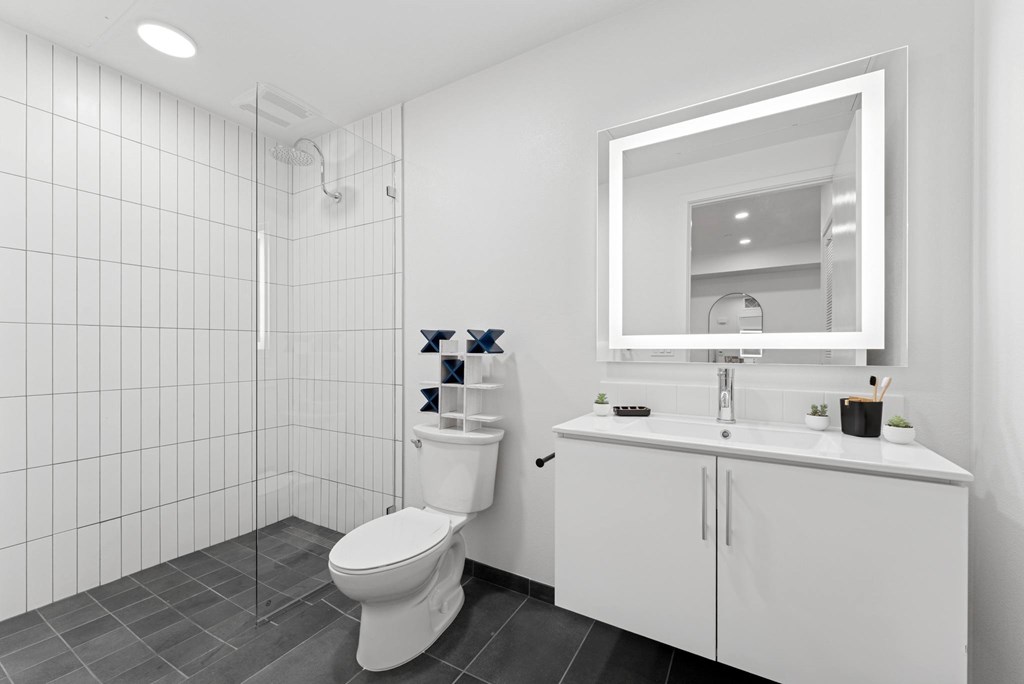 OnyxOnPark_SanDiego_CA_Model_1BR_ A white bathroom with a toilet, sink, and mirror.
