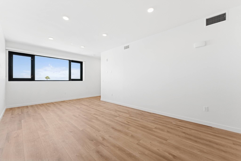 OnyxOnPark_SanDiego_CA_Vacant_2BR_ A room with wooden flooring and a window showing a blue sky with clouds.