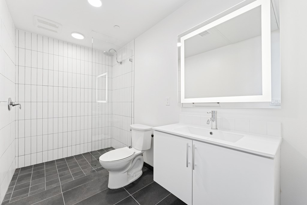 OnyxOnPark_SanDiego_CA_Vacant_2BR_ A white bathroom with a toilet, sink, and mirror.