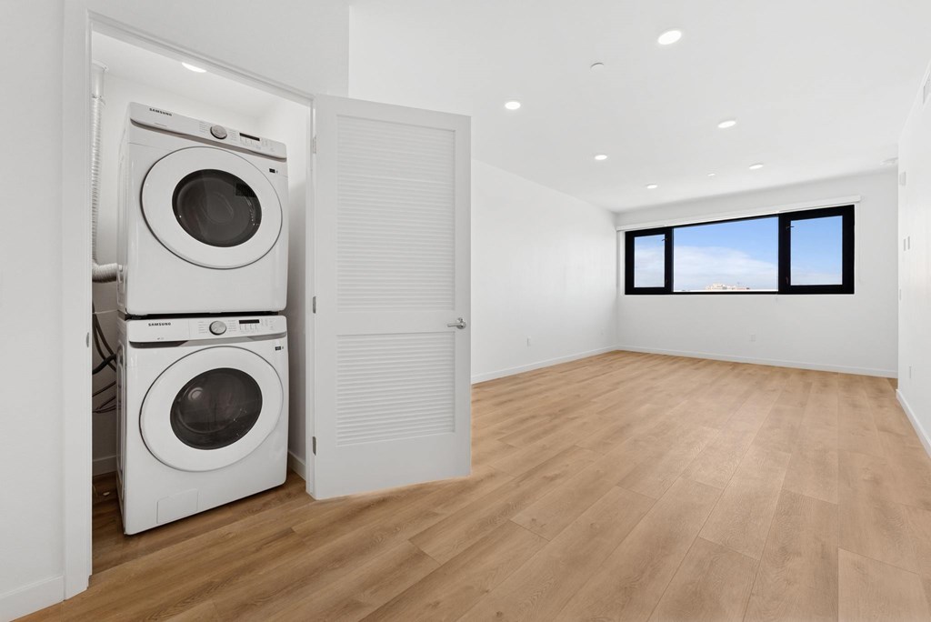 OnyxOnPark_SanDiego_CA_Vacant_2BR_ A white washing machine is in a room with wooden floors and a window.