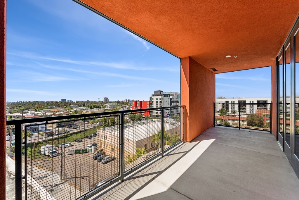 A balcony with a black railing and a view of a parking lot and buildings.