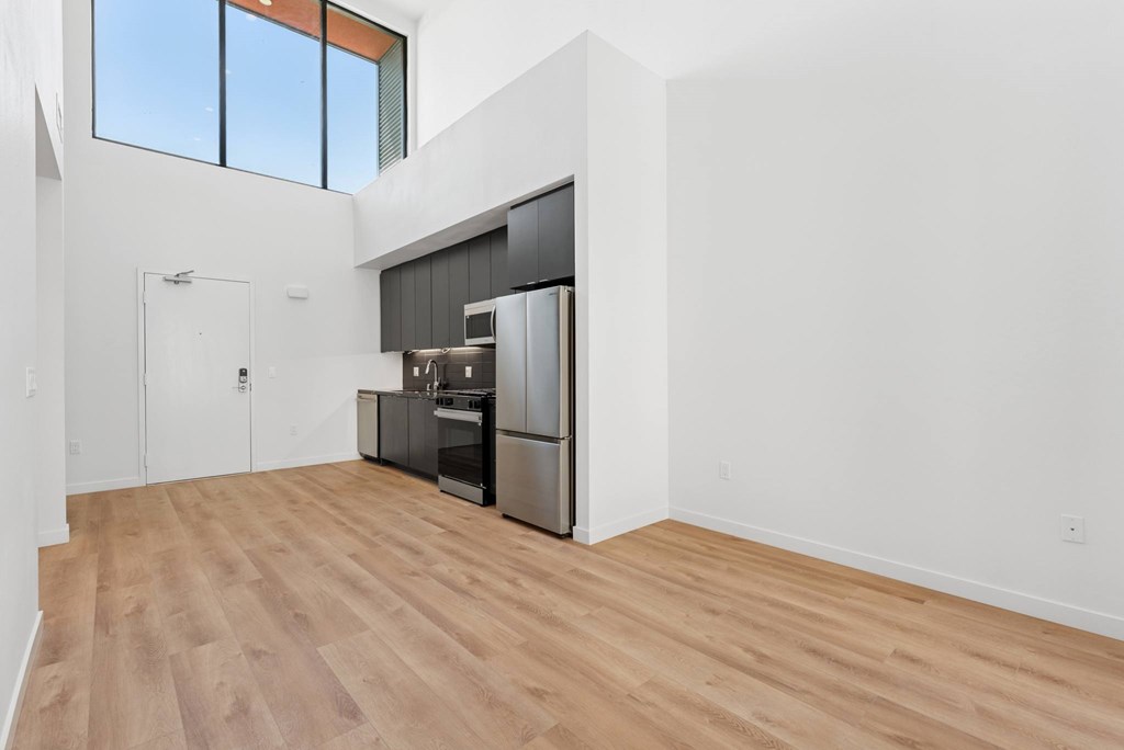 OnyxOnPark_SanDiego_CA_Vacant_Penthouse_A_OnyxOnPark_SanDiego_CA_Vacant_Penthouse_A_A kitchen with a refrigerator, oven, and sink is in a room with wooden floors and white walls.