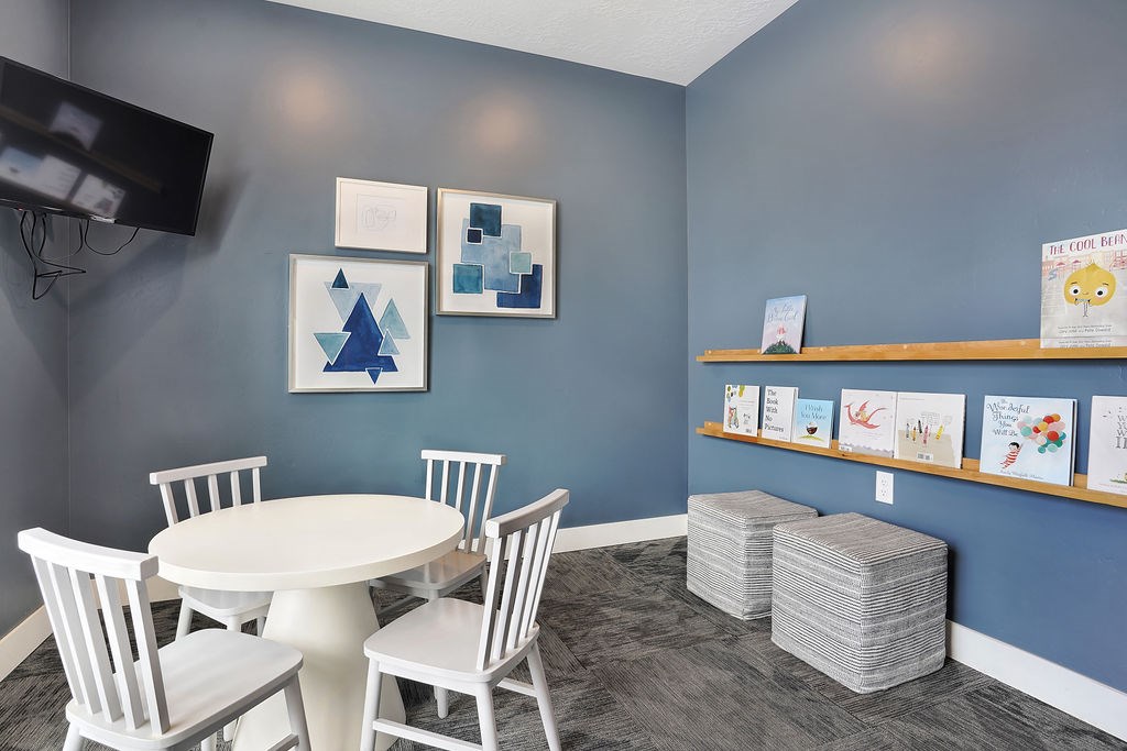 Alvera at the Meadows room with a white table and chairs, a TV, and some artwork  and books on the wall.