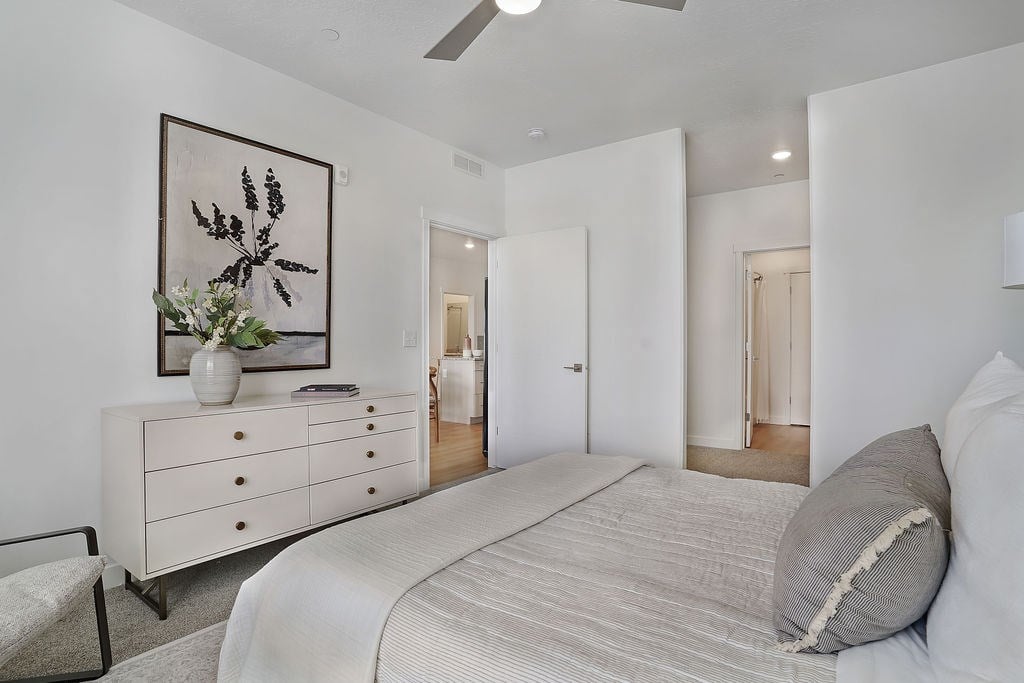 Alvera at the Meadows bedroom with a large bed, a dresser with a vase of flowers, and a framed picture on the wall.