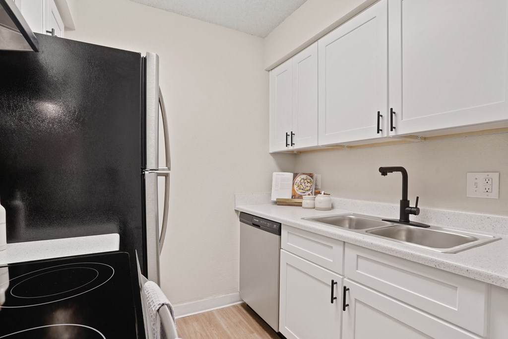 a kitchen with white cabinets and a black refrigerator and sink