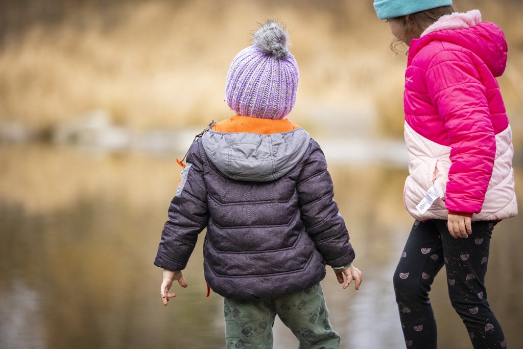 A child in a purple hat and jacket is walking with an adult.