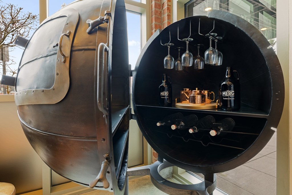 A large metal container with a glass door is open, revealing several wine bottles inside.