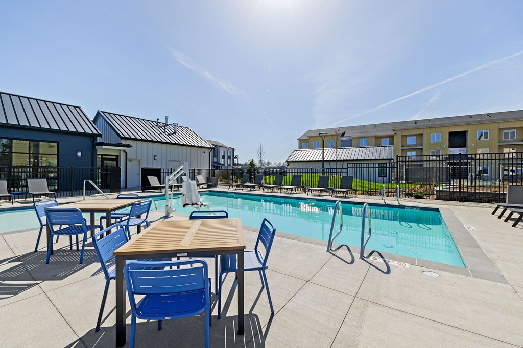 A sunny day at the pool with blue chairs and a wooden table.
