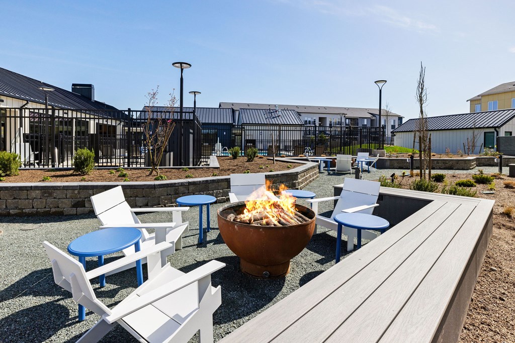 A fire pit sits in the middle of a patio with blue and white chairs surrounding it.