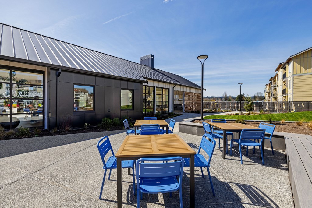 A patio with blue chairs and tables is in front of a building.