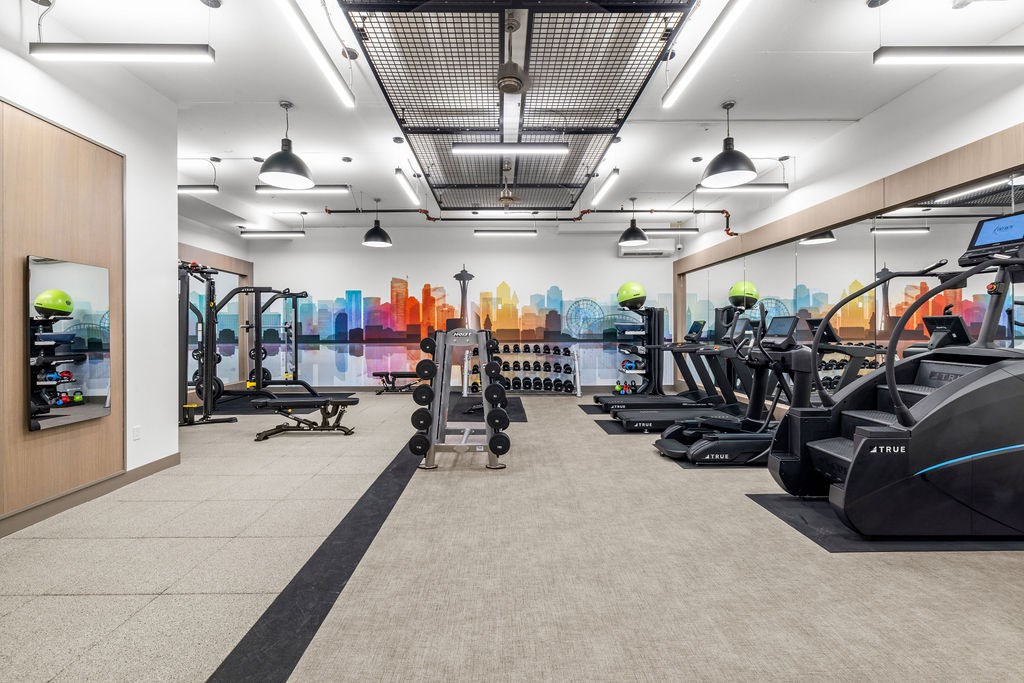 A gym with treadmills, weights, and a cityscape mural on the wall.