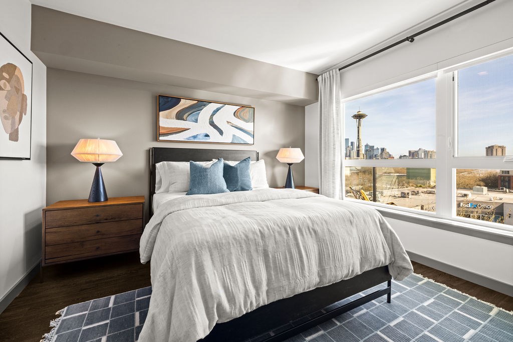 A bedroom with a large bed, two lamps, and a view of the city.