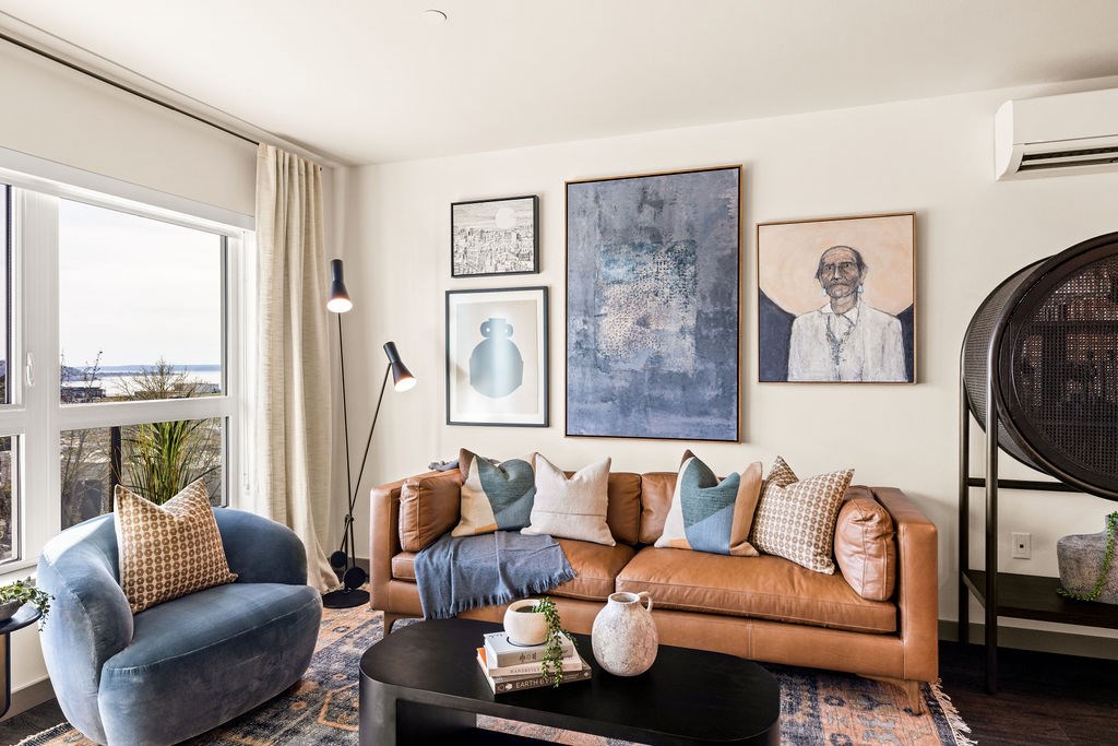 A living room with a blue chair, a brown couch, and a painting on the wall.