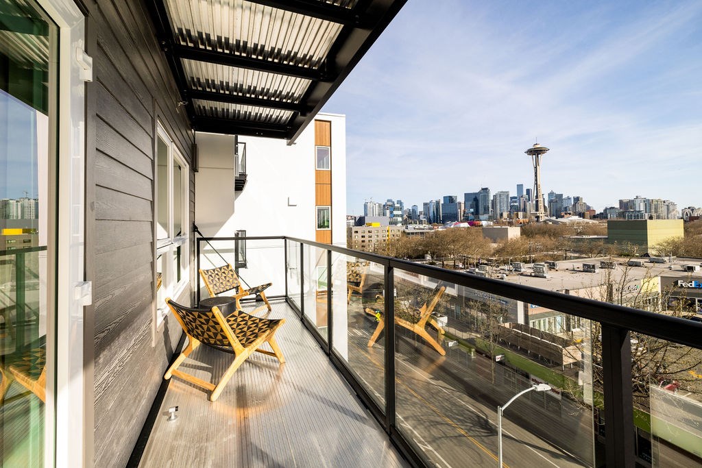 A balcony with two chairs and a table overlooks a cityscape.