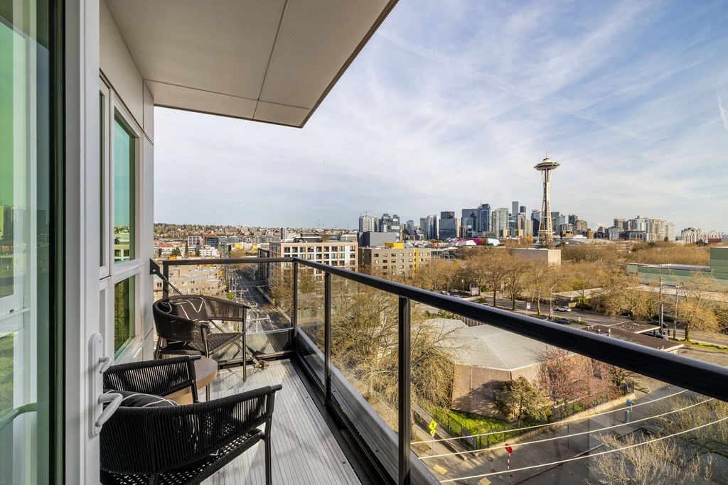 A balcony with chairs and a table overlooks a cityscape.