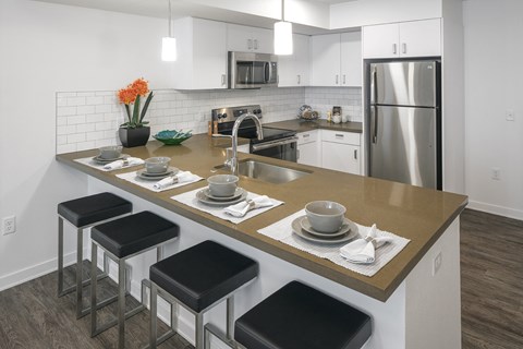 a kitchen with a large island with stools and a stainless steel refrigerator