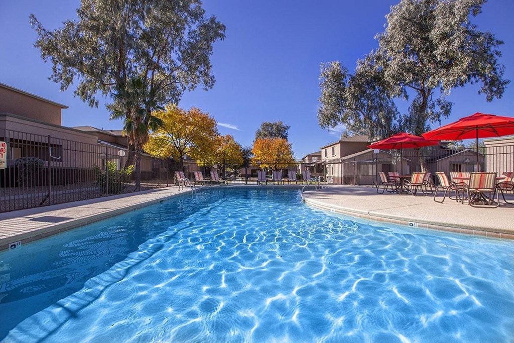 A swimming pool surrounded by trees and chairs with umbrellas.