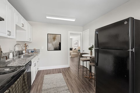 A black refrigerator stands in a kitchen with white cabinets and a rug on the floor.
