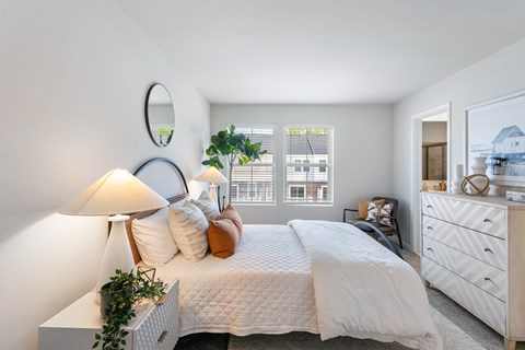 A well-lit bedroom with a large bed, a white dresser, and a mirror on the wall.