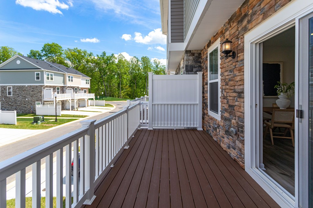A wooden deck with a white railing and a sliding glass door leading to a patio.