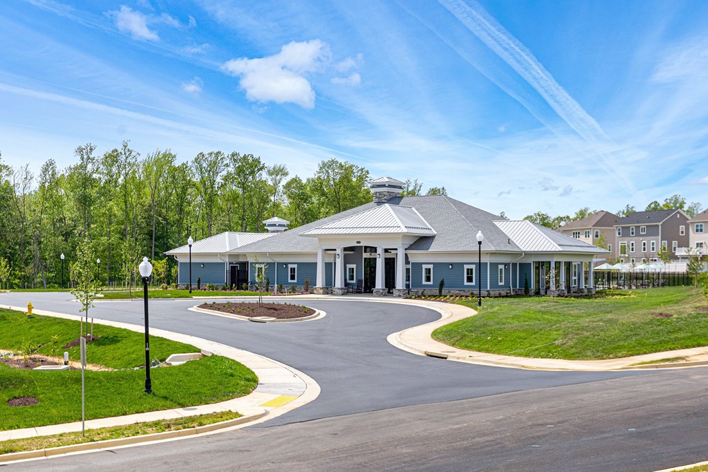 A large building with a grey roof is surrounded by a grassy area and a paved road.
