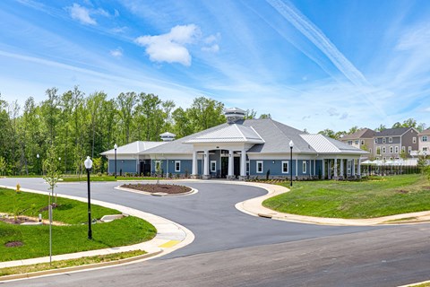 A large building with a grey roof is surrounded by a grassy area and a paved road.