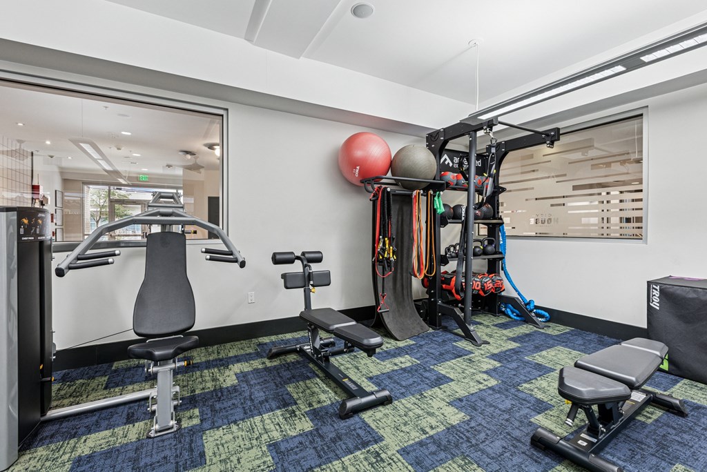 A gym with a variety of equipment including a weight bench, a leg press machine, and a cable machine.