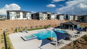 A swimming pool surrounded by chairs and umbrellas in front of apartment buildings.