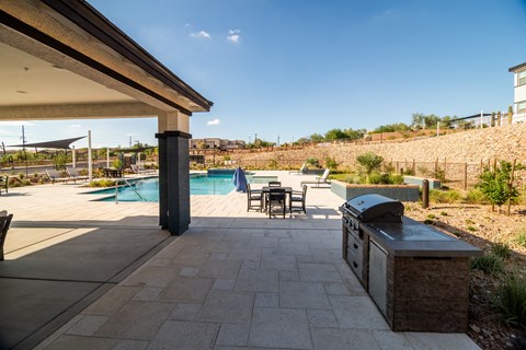 A patio with a grill and a pool in the background.