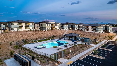 A swimming pool is surrounded by a fence and a parking lot in front of apartment buildings.
