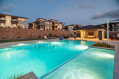 A swimming pool in a backyard with a stone wall and a building in the background.
