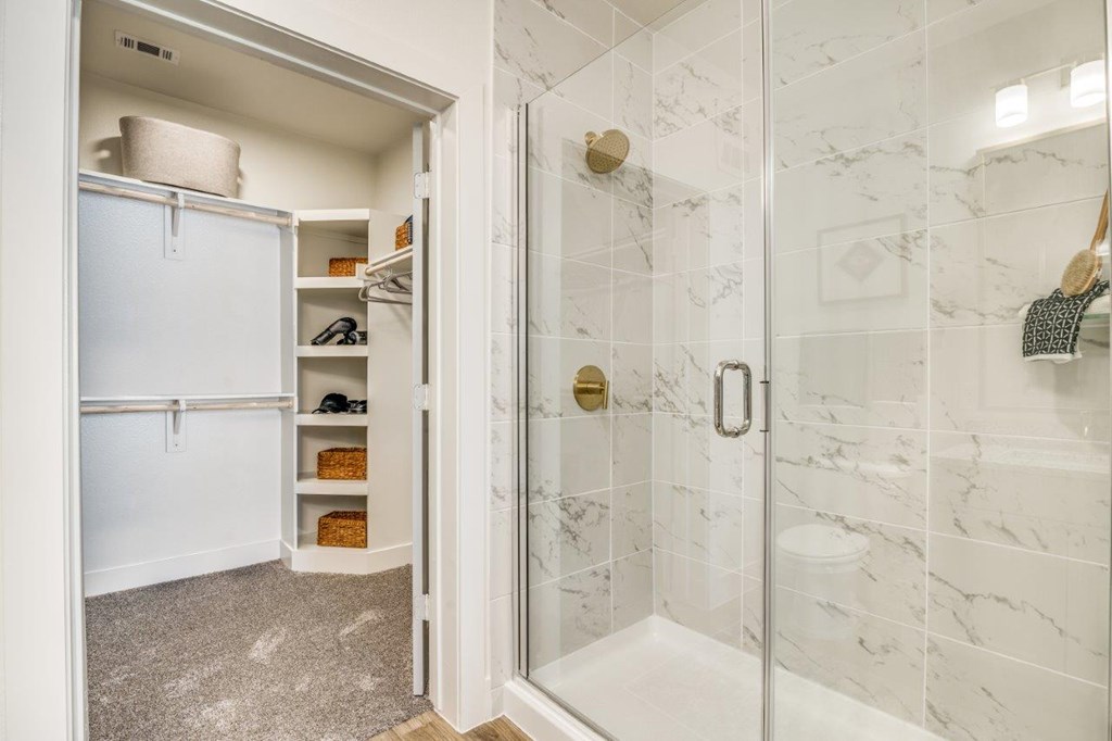 A white fridge is in a small kitchen next to a walk in shower.