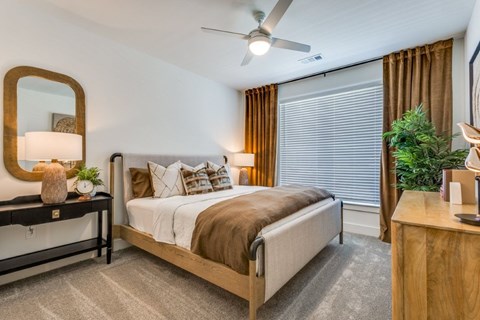 A bedroom with a bed, a mirror, a nightstand, and a plant.