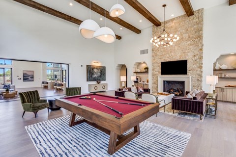 A pool table is in the middle of a room with a stone fireplace and a TV.