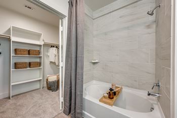 A bathroom with a white tub and grey tiles.