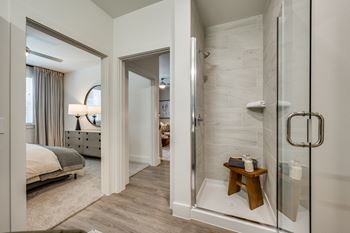 A bathroom with a walk-in shower and a bedroom with a bed and a nightstand.